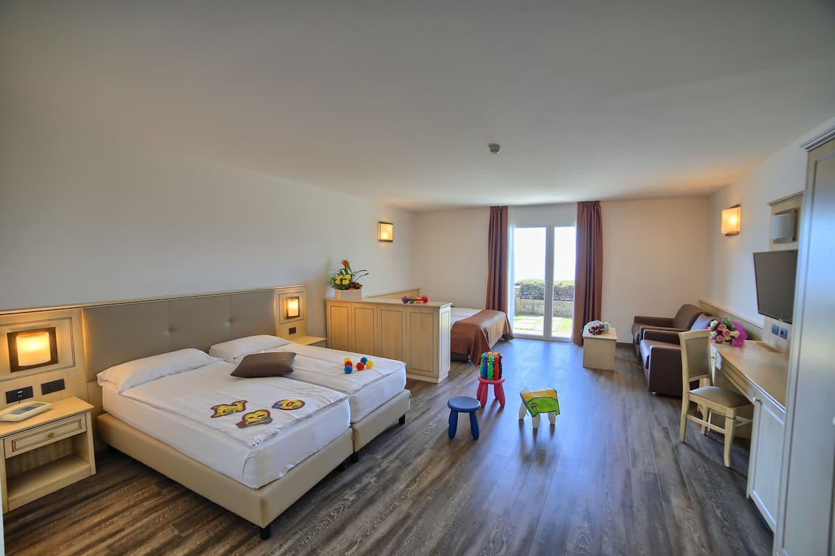 A hotel room with two beds, a desk, a chair, a TV, and a small table with a flower vase.