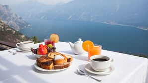Een ontbijttafel met koffie, sap en gebak, met uitzicht op een bergmeer.