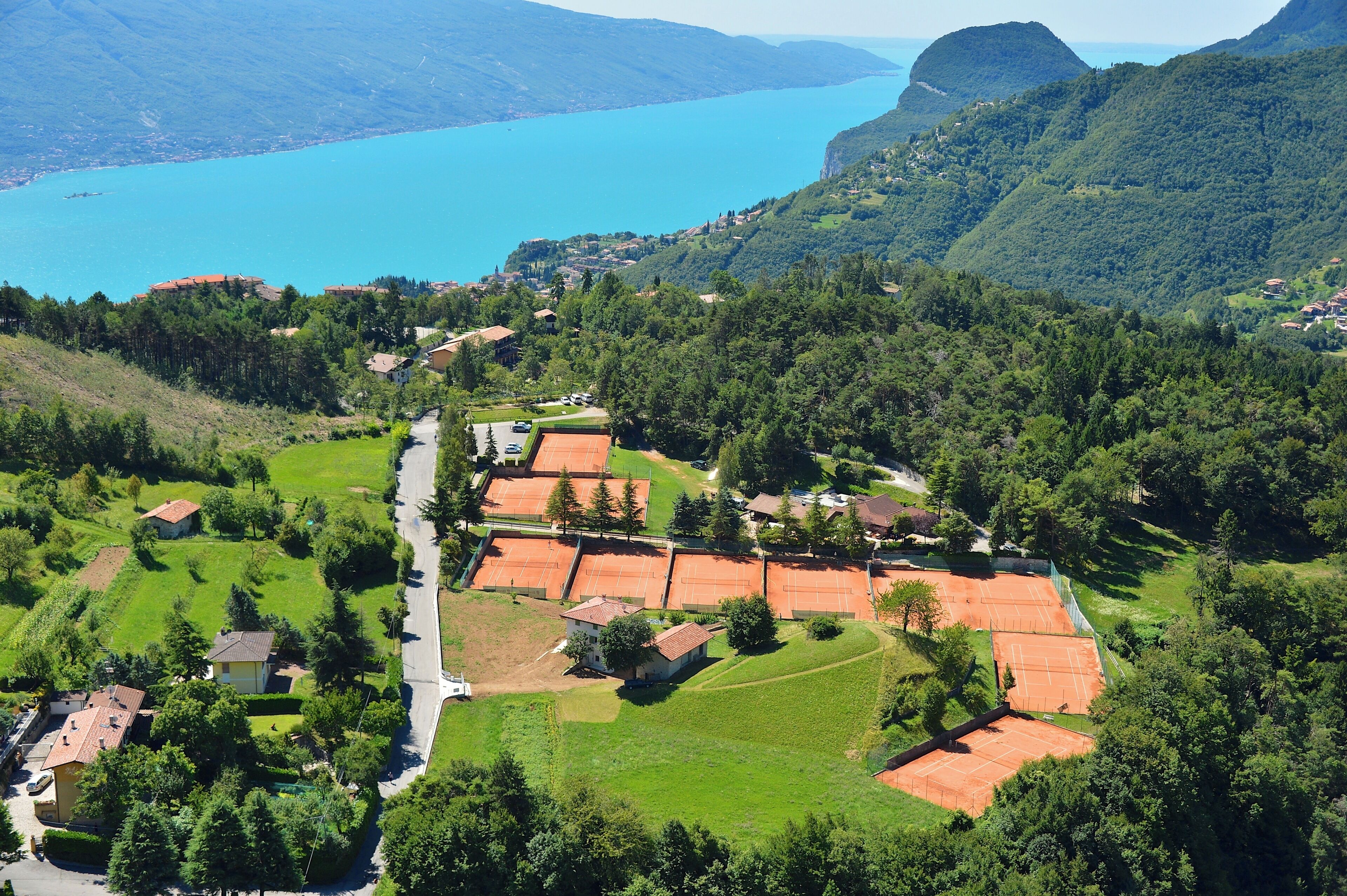 Vista aérea de una zona residencial con casas, canchas de tenis y un lago al fondo.