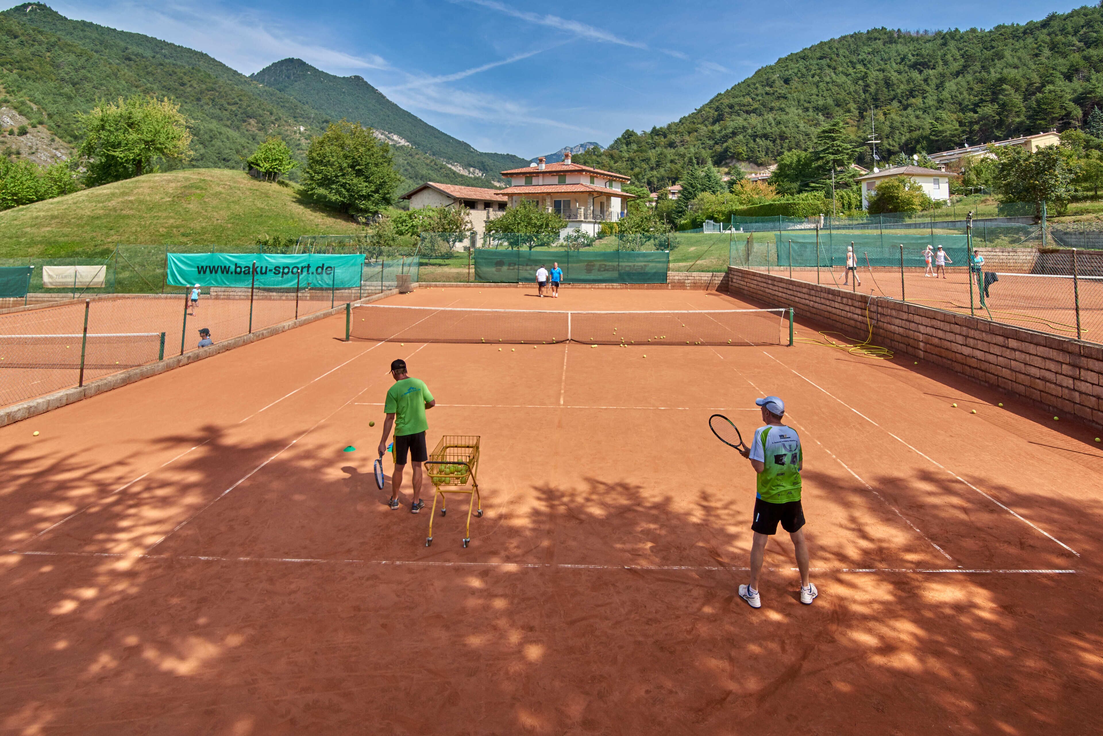 Una cancha de tenis con red, rodeada de una cerca, y un edificio al fondo.