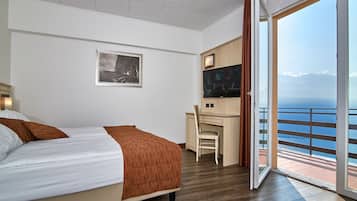 Una camera d'albergo con un letto, una scrivania con una sedia, una televisione e un'ampia finestra vista mare.