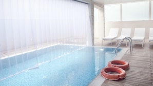 Une piscine à l’eau claire, avec une terrasse en bois et des chaises longues.