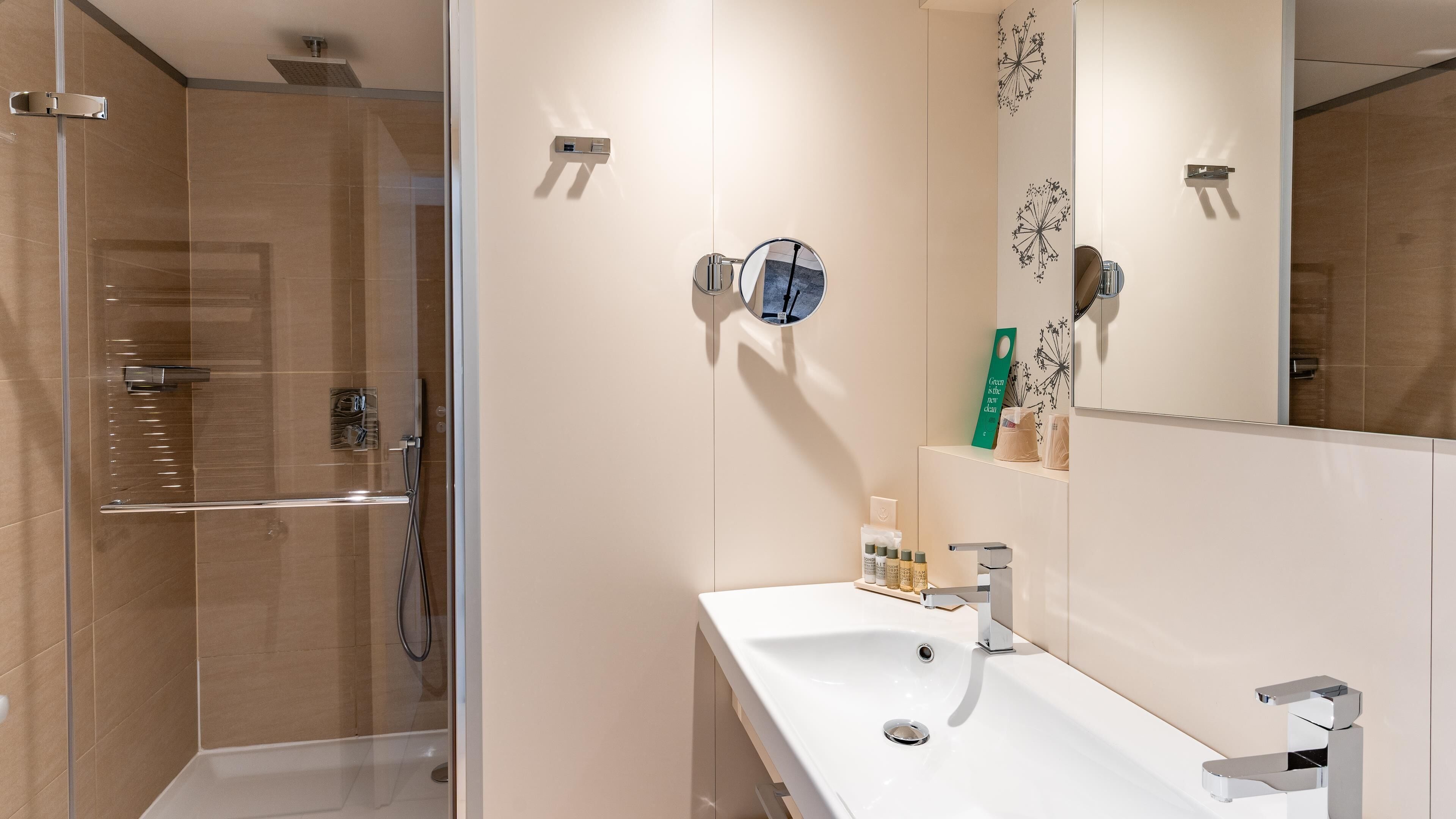 A modern bathroom with a glass shower enclosure, a white sink with a chrome faucet, and a mirror with a decorative wall piece.