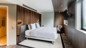 A modern bedroom with a large bed, a wooden panel wall, a chair, and a window.