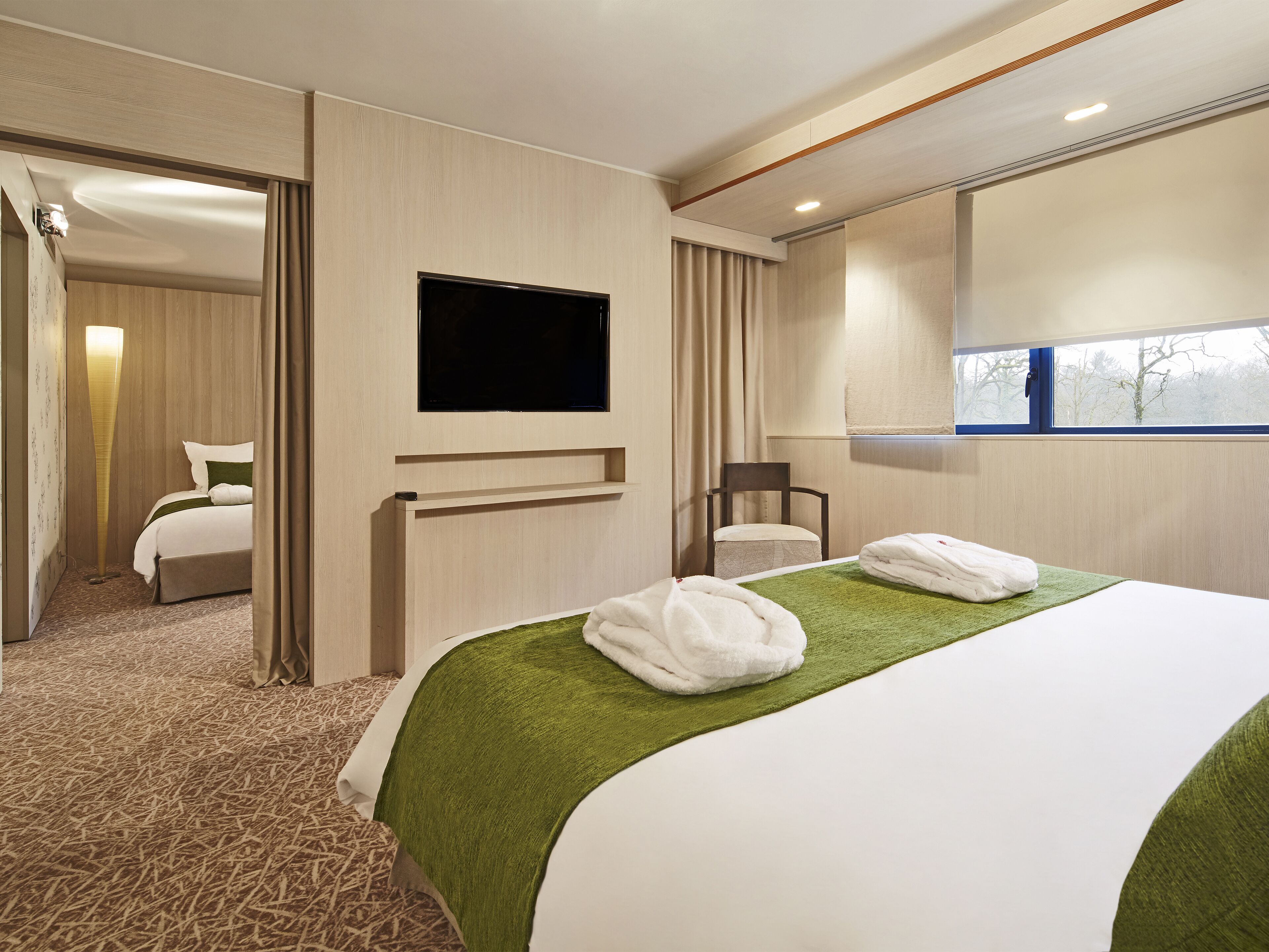 A hotel room with a bed, a TV, a chair, and a window.