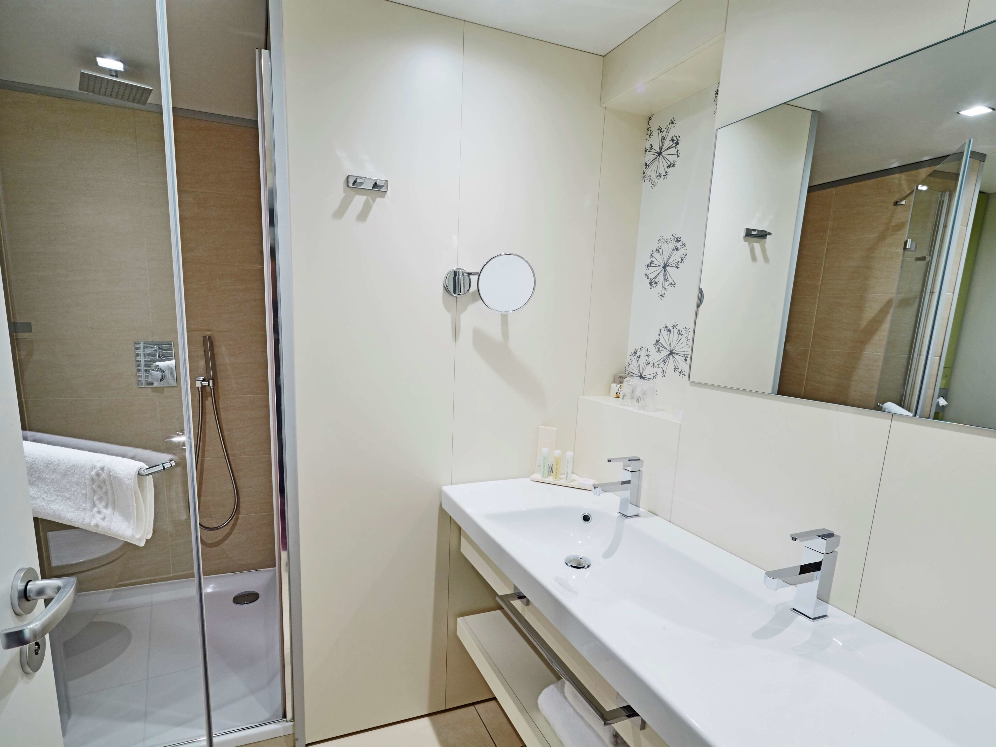 A modern bathroom with a glass-enclosed shower, a white sink with a mirror above it, and a towel rack.