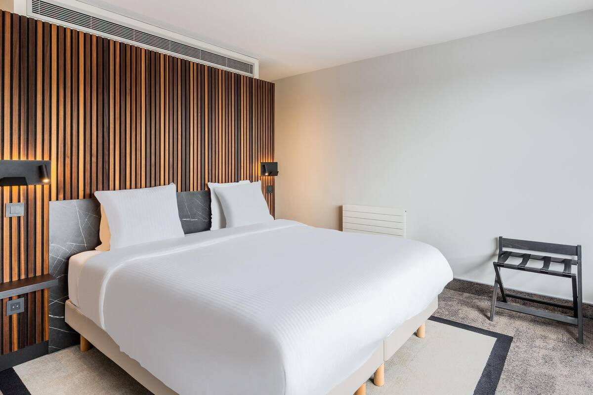 A modern hotel room with a large bed, wooden panel wall, and a small side table.