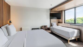 Quarto de hotel moderno com uma cama grande, duas camas menores, uma televisão e uma janela com vista.