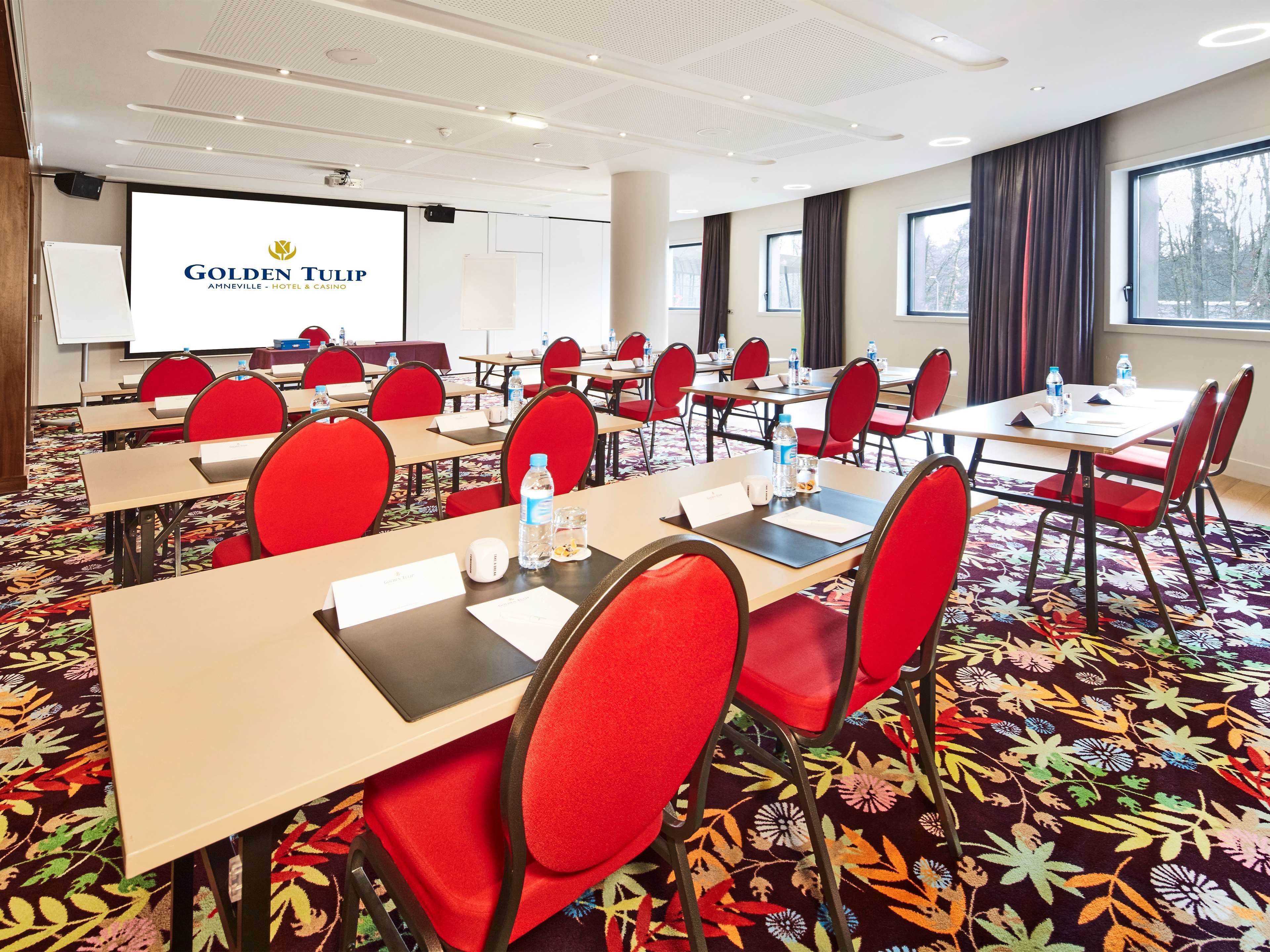 A conference room with red chairs, tables, and a projector screen displaying "Golden Tulip".