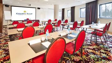 A conference room with red chairs, tables, and a projector screen displaying "Golden Tulip".