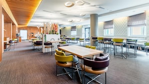 A spacious dining area with multiple tables and chairs, a kitchen area, and a decorative wall with plants.