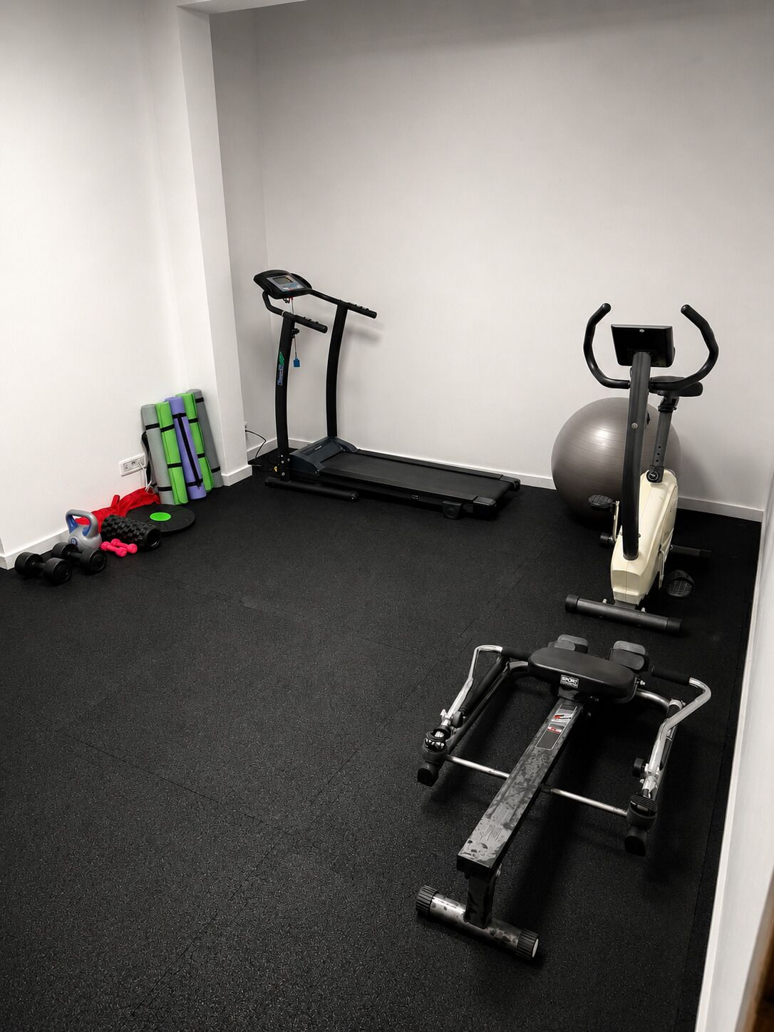 Un gimnasio con cinta de correr, elíptica, bicicleta estática y varios pesas.