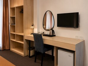 Habitación de hotel con un escritorio de madera, un espejo, un televisor y un refrigerador compacto.