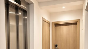 A hallway with a metallic elevator, a wooden door with a keycard lock, and a carpeted floor. - Garni Hotel Fineso (Budva)