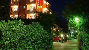 Un hotel de varios pisos con un llamativo letrero que dice 'HOTEL', un coche rojo estacionado adelante y una entrada bien iluminada.