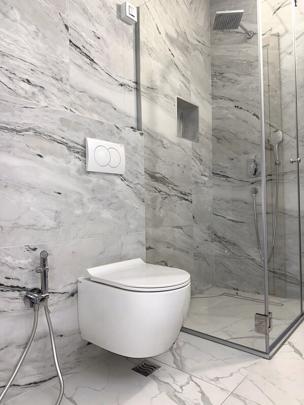 Un baño con inodoro blanco, ducha con cerramiento de vidrio y paredes de mármol.
