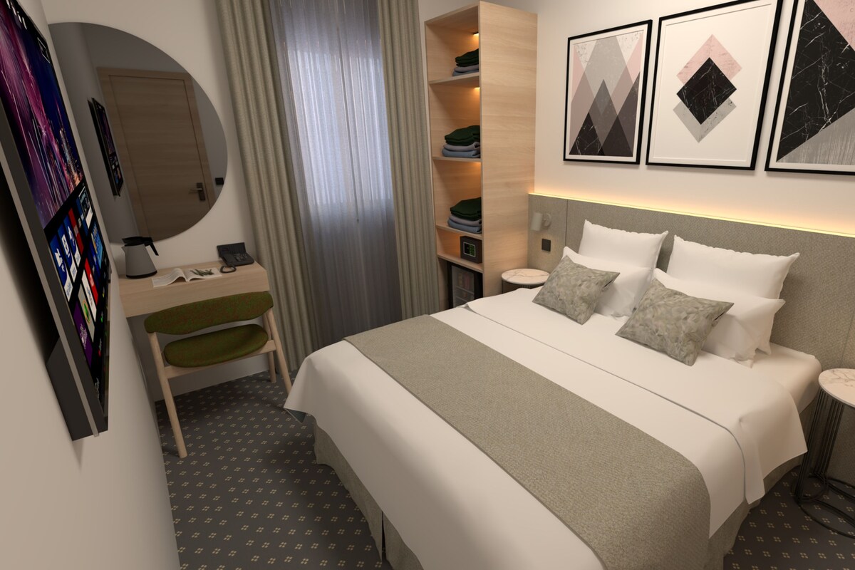 Una habitación de hotel moderna con una cama, mesitas de noche, un escritorio, una silla, un armario y obras de arte en la pared.