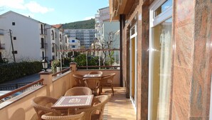 Un balcón con mobiliario de mimbre y suelo de baldosas, con vistas a una calle y edificios.