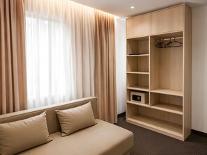Una habitación con cama, armario y ventana con cortinas.