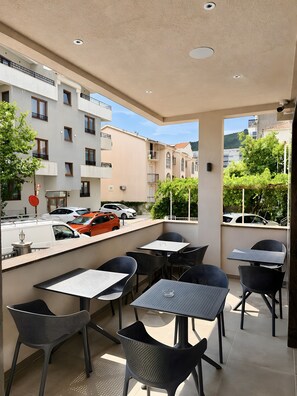 An outdoor seating area with tables and chairs, a view of the street, and buildings in the background. - Garni Hotel Fineso (Budva)