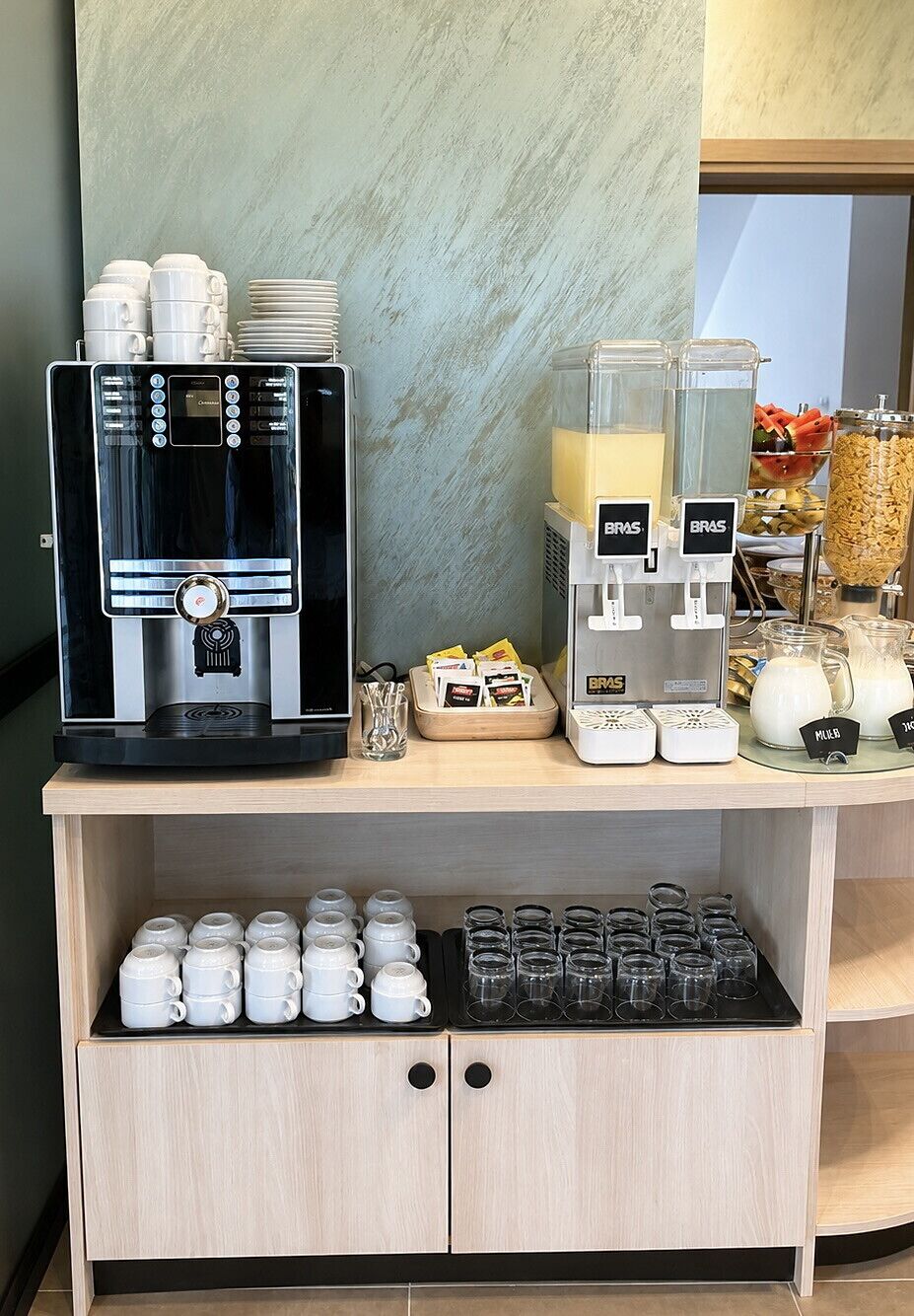 Una estación de café con dos máquinas de café, un dispensador de leche y una variedad de tazas y vasos.