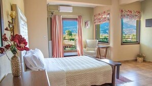 A bedroom with a bed, a chair, a small table, a window with a view, and a decorative plant.