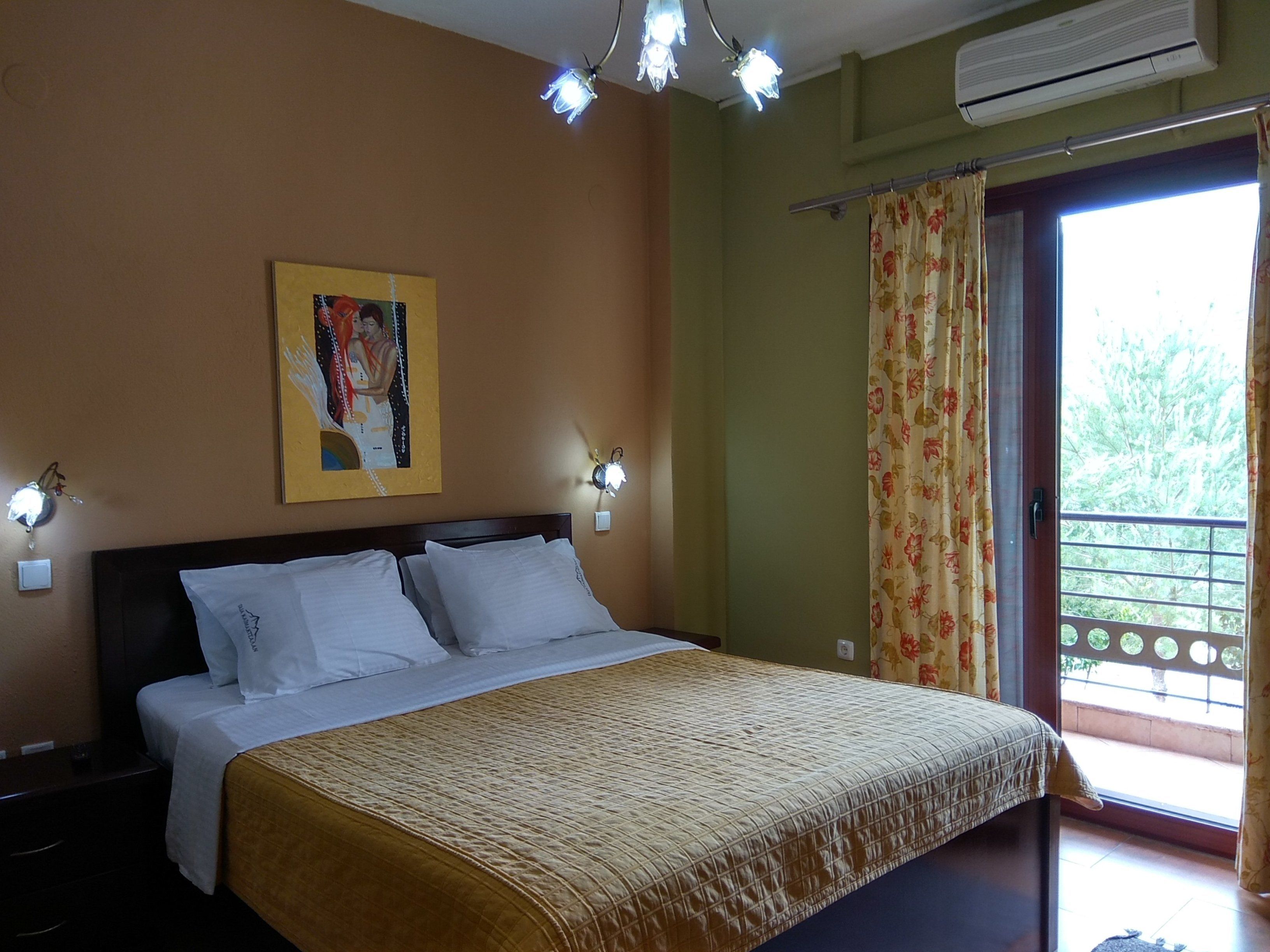 Una habitación de hotel con cama, un cuadro en la pared, una ventana con cortinas y un equipo de aire acondicionado.