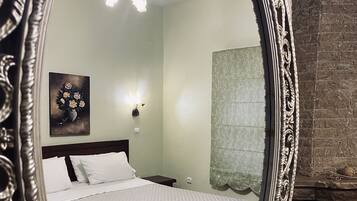 A bedroom with a bed, a nightstand, a wall-mounted lamp, a painting, and a fireplace.