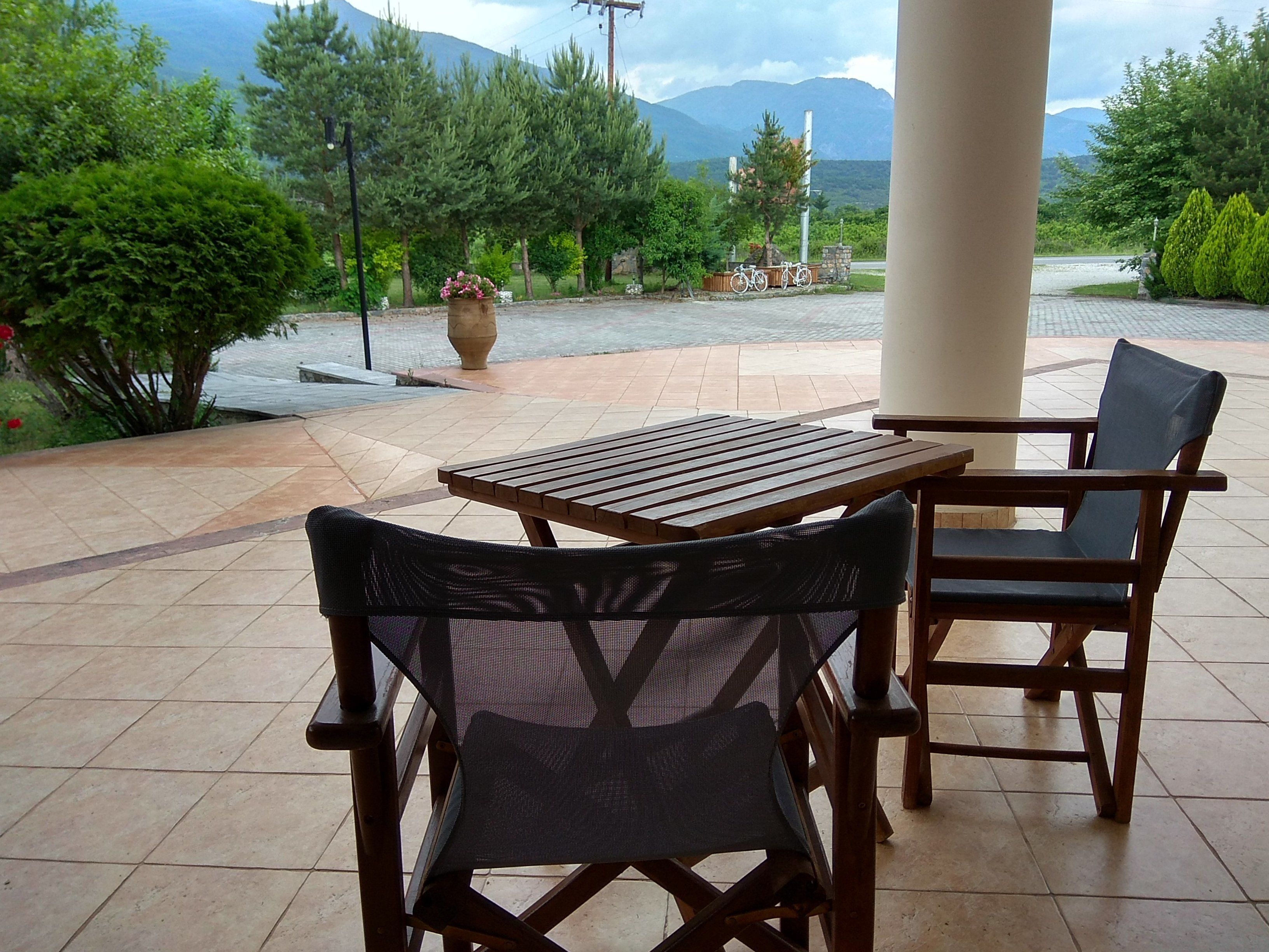 Patio esterno con tavolo e sedie in legno, immerso nel verde e con vista sulle montagne.