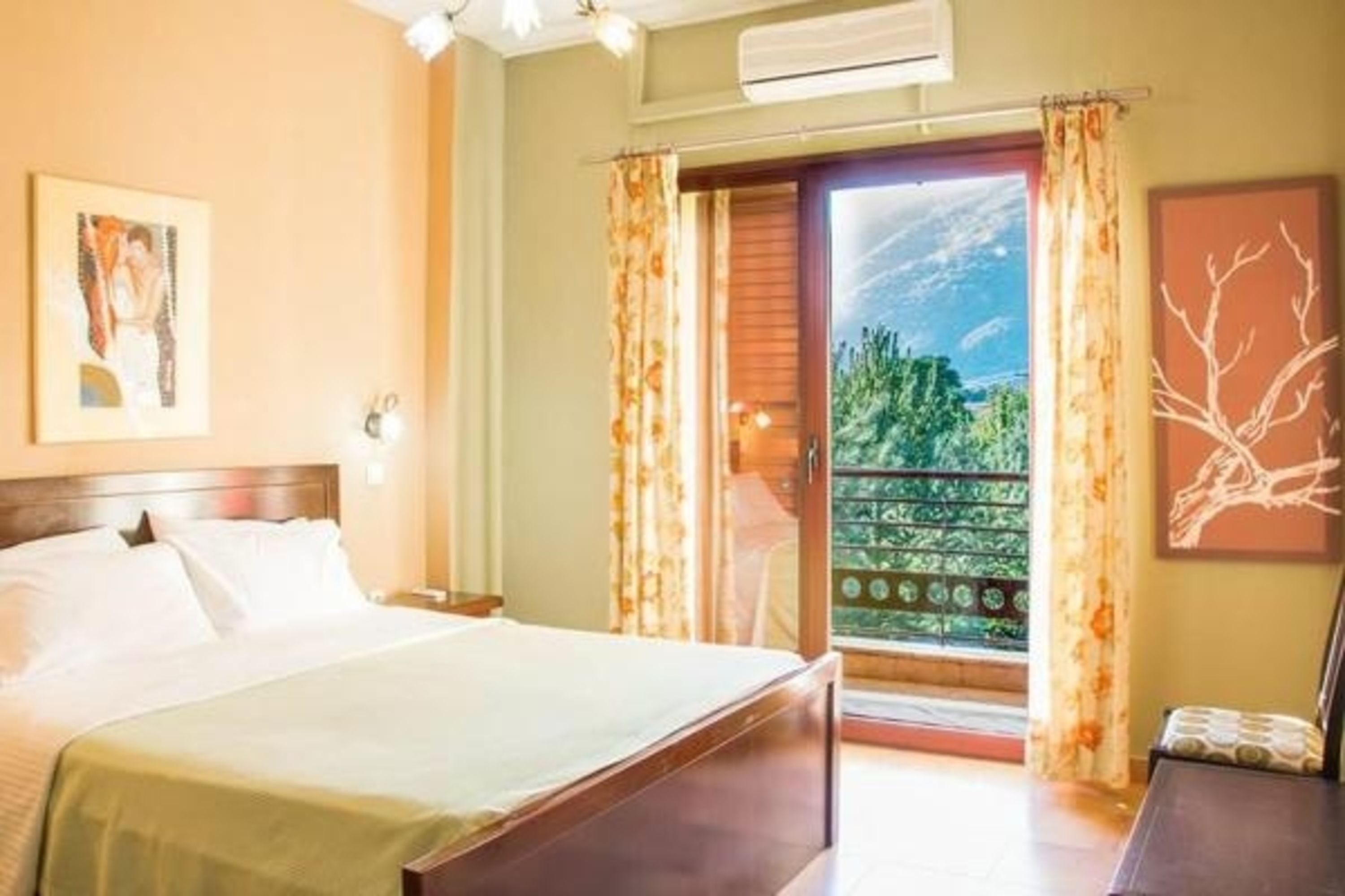 A hotel room with a bed, a nightstand, a window with curtains, and a view of greenery outside.