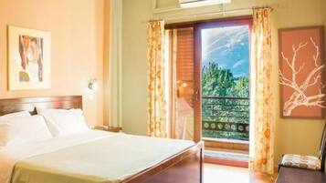 A hotel room with a bed, a nightstand, a window with curtains, and a view of greenery outside.