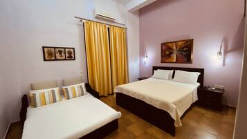 Una habitación de hotel con dos camas, un ventanal con cortinas amarillas, un aire acondicionado y un cuadro en la pared.