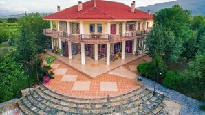 A two-story building with a red roof, a balcony, and a circular stone staircase leading to the entrance.
