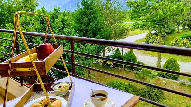 A balcony with a breakfast setup including croissants, a bowl of yogurt with fruit, and a cup of coffee.