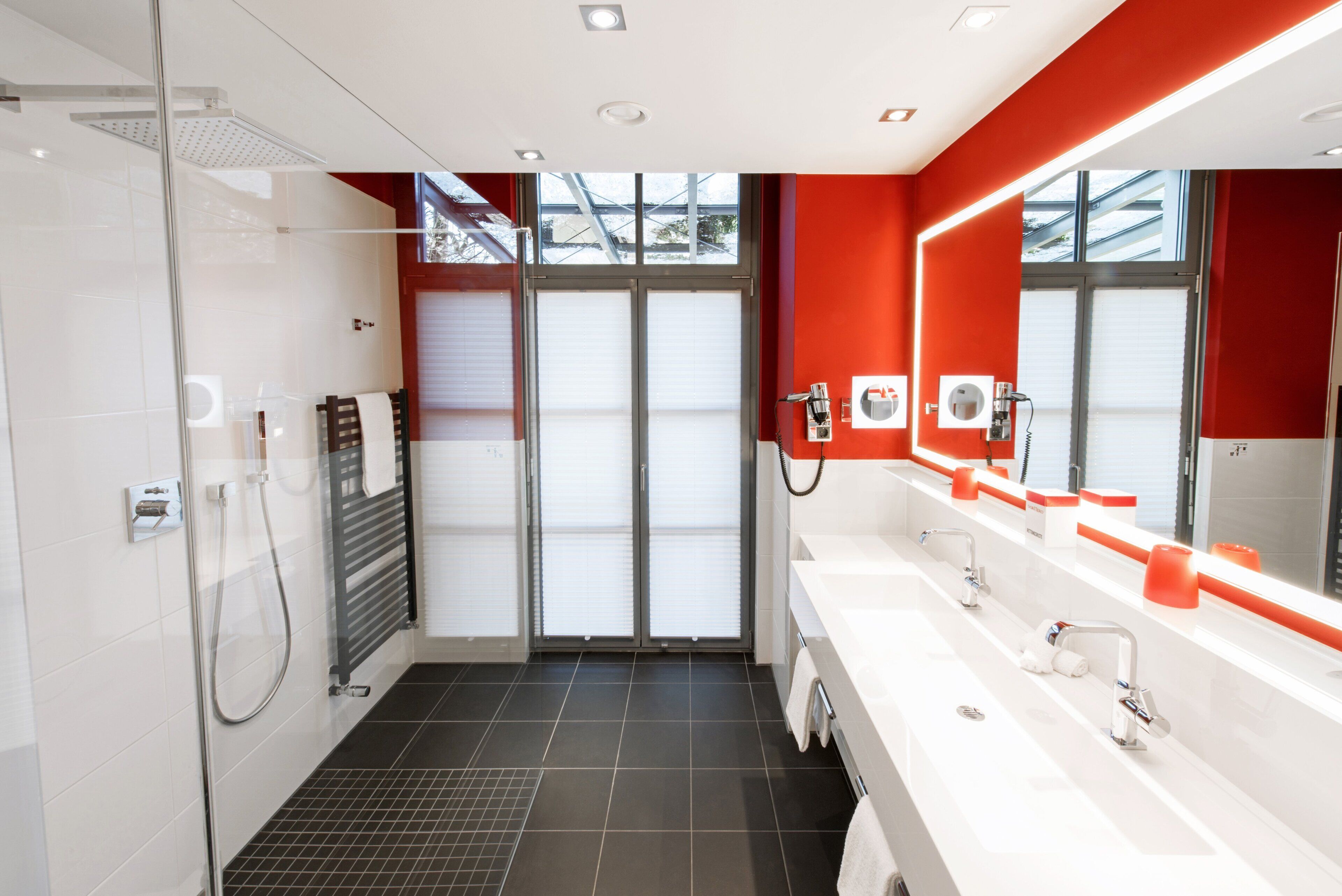 A modern bathroom with a glass shower enclosure, a large mirror, and a white sink with a red accent wall.