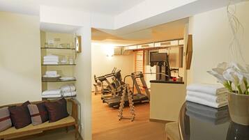 A home gym with exercise equipment, a sofa with cushions, and a glass shelf with towels.