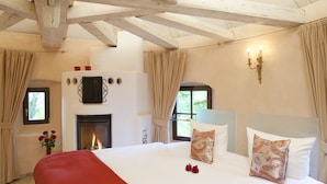 A bedroom with a fireplace, a bed with patterned pillows, and a window with curtains.