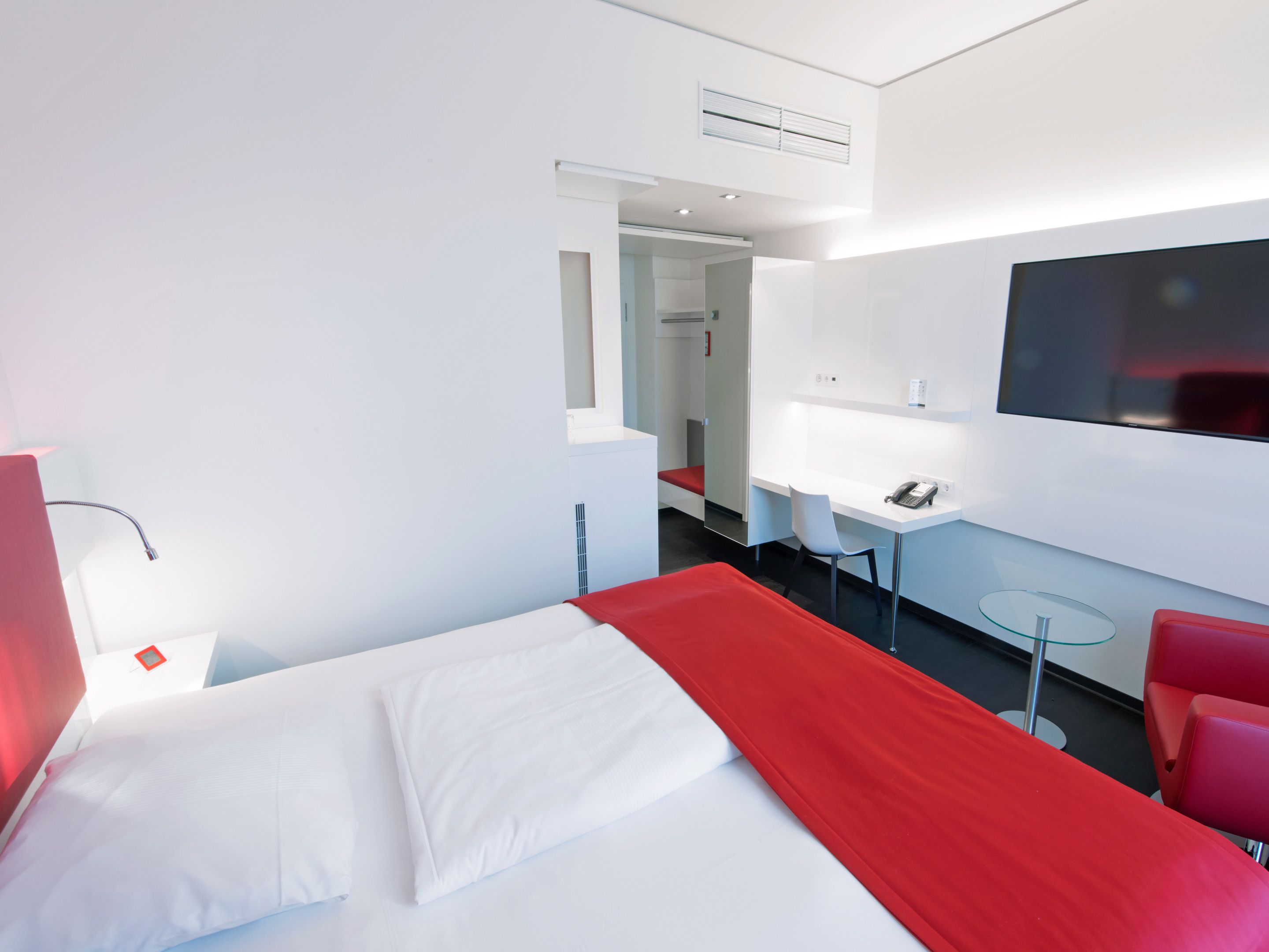 A modern hotel room with a bed, a desk, a chair, a TV, and a small table.
