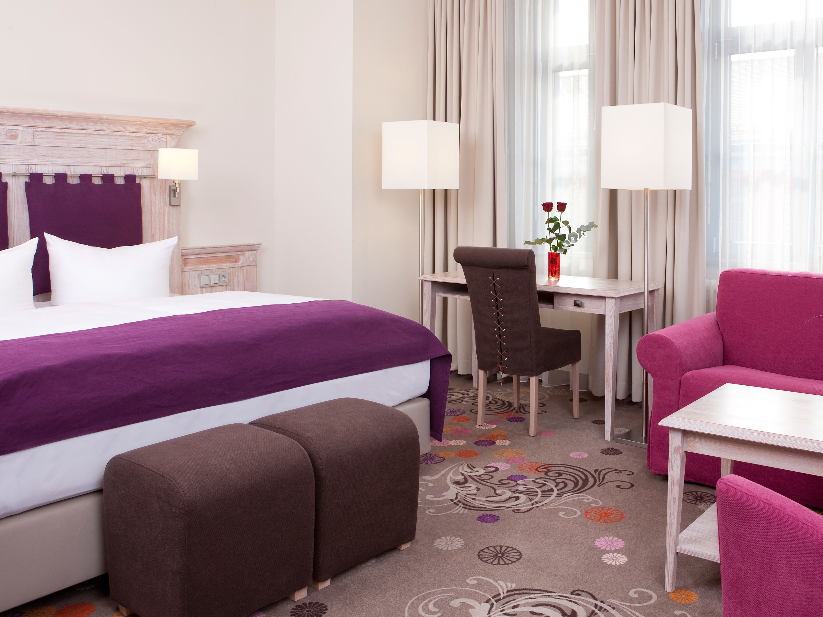 A hotel room with a bed, a desk, a chair, a sofa, and a carpet with floral patterns.