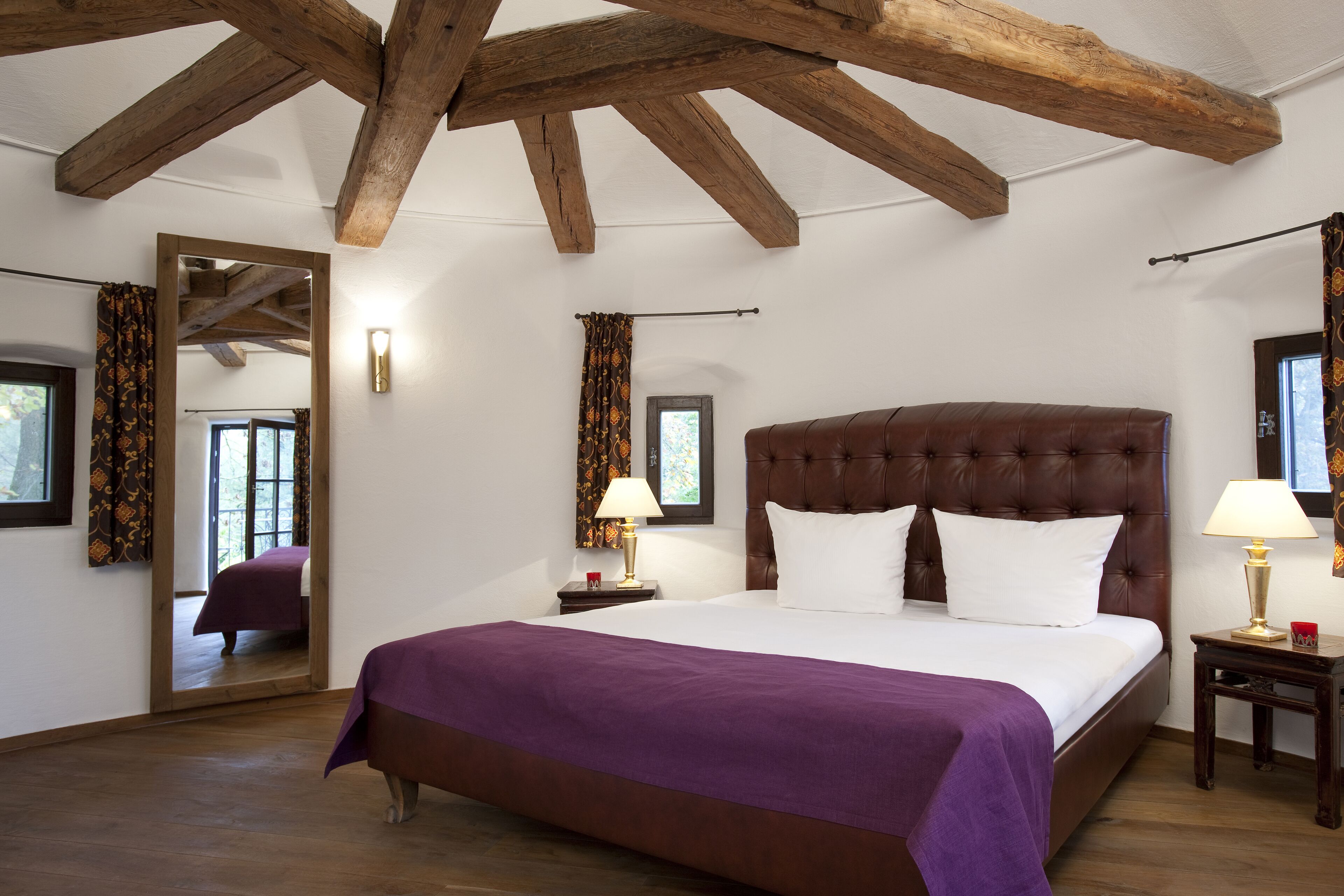 Un dormitorio con una cama grande, vigas de madera, un espejo y dos mesitas de noche con lámparas.