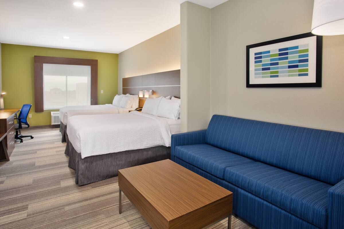 A hotel room with a bed, a blue sofa, a wooden coffee table, and a desk with a chair.