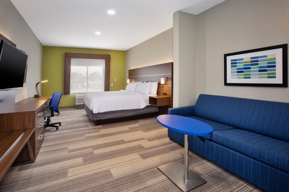 A hotel room with a bed, a blue sofa, a desk with a chair, a TV, and a framed picture on the wall.