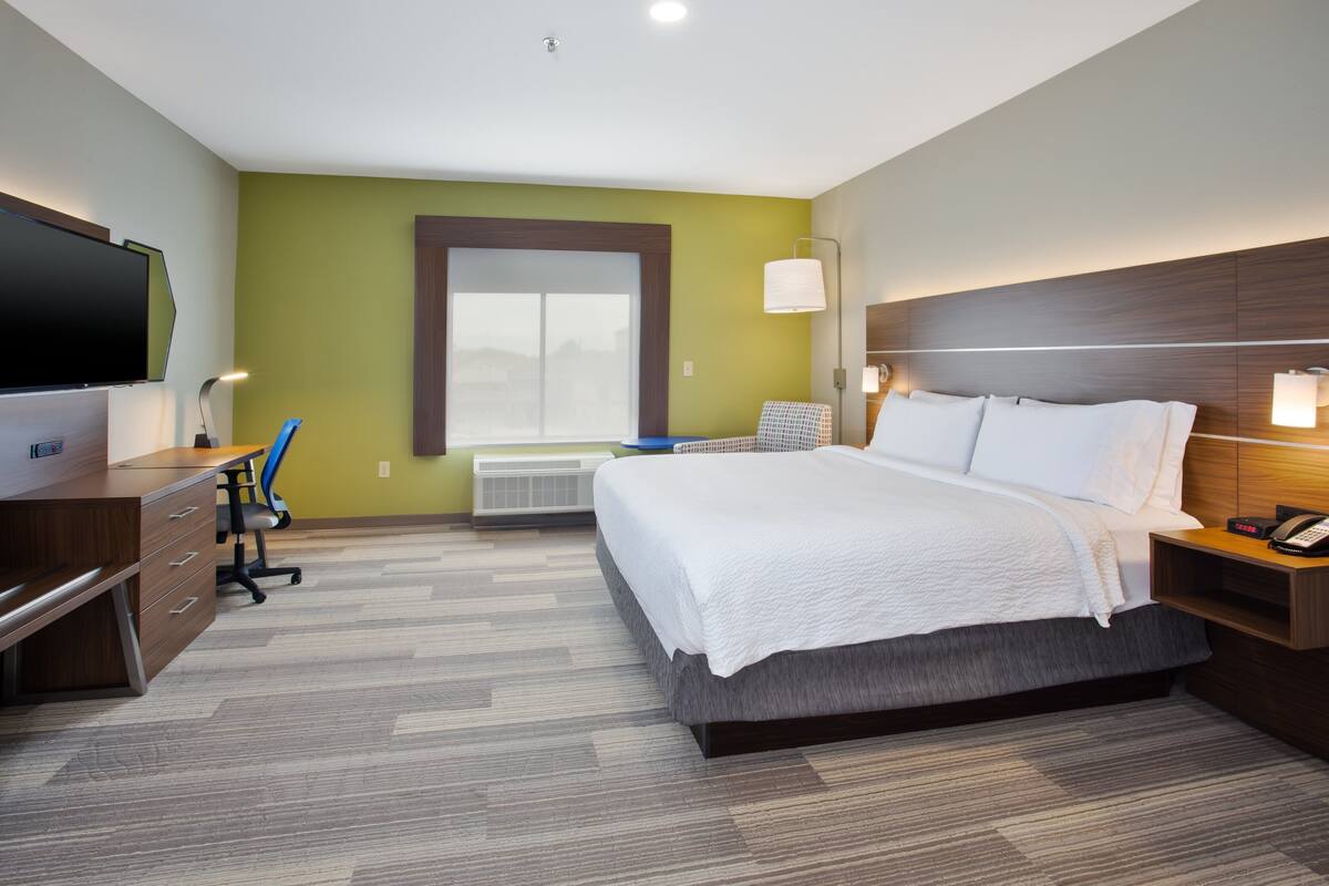 A hotel room with a bed, desk, chair, TV, and a window with a view.
