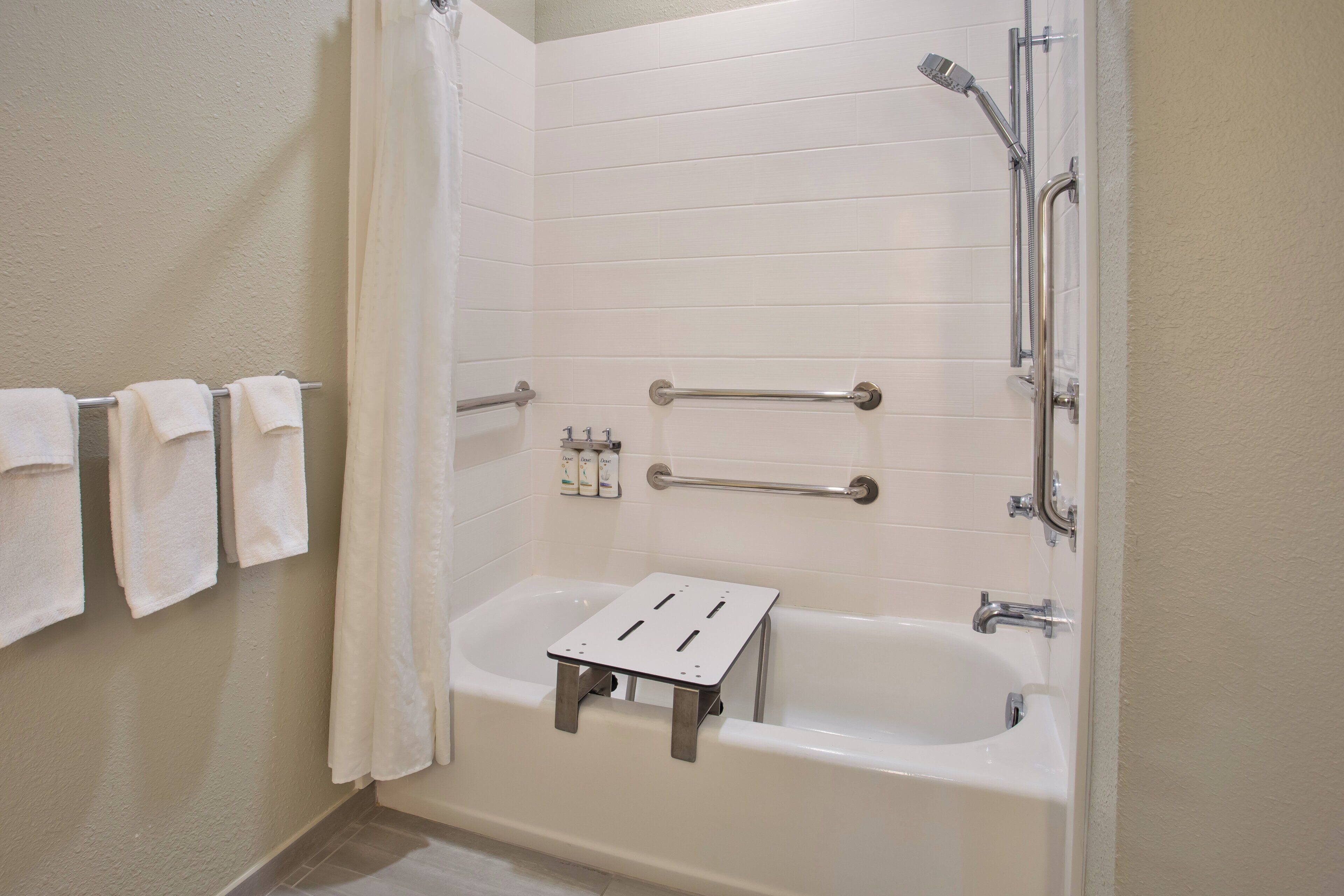 Un baño con bañera, ducha y un taburete pequeño. Hay toallas colgadas en un perchero y una cortina de ducha.