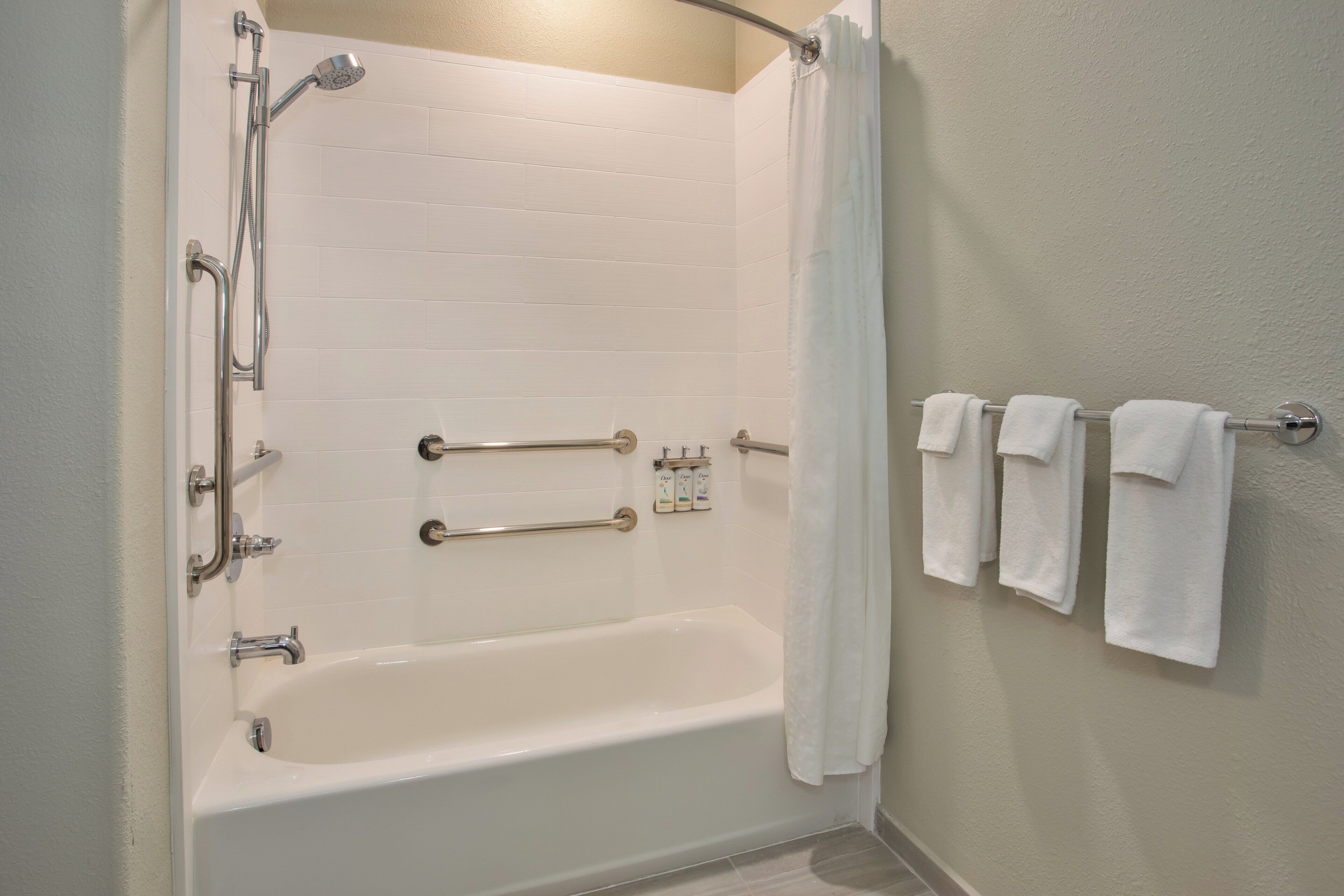 Ett standardbadrum på ett hotell med badkar, dusch, handtag och en handduksställning.