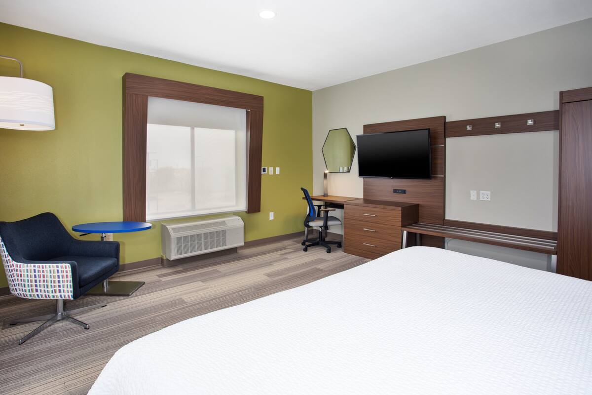 A hotel room with a large bed, a desk with a chair, a television, and a window.