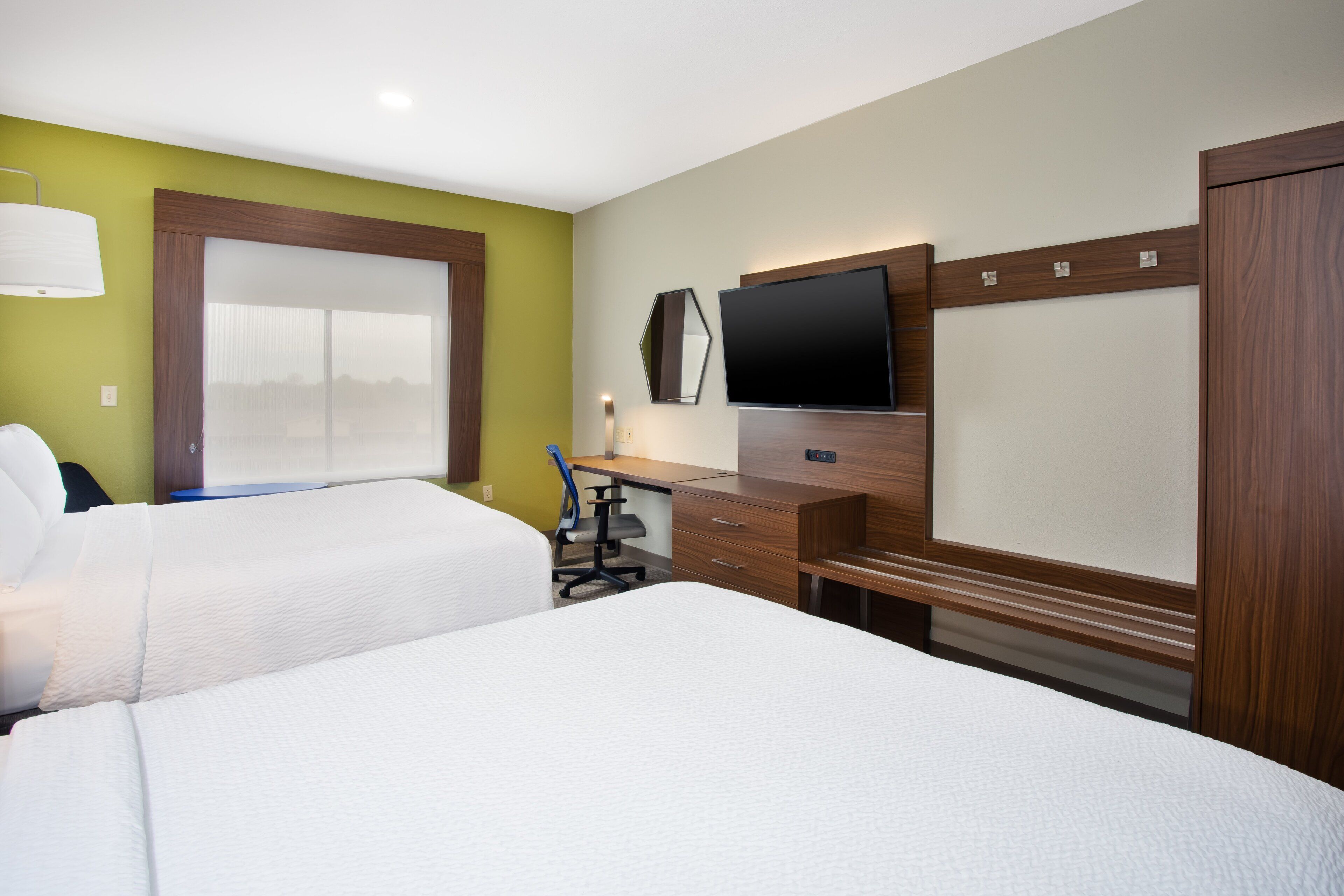 A hotel room with two beds, a desk, a chair, a TV, and a large window.