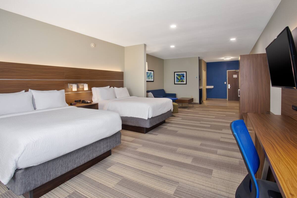 A hotel room with two beds, a desk, a TV, and a bathroom visible in the background.