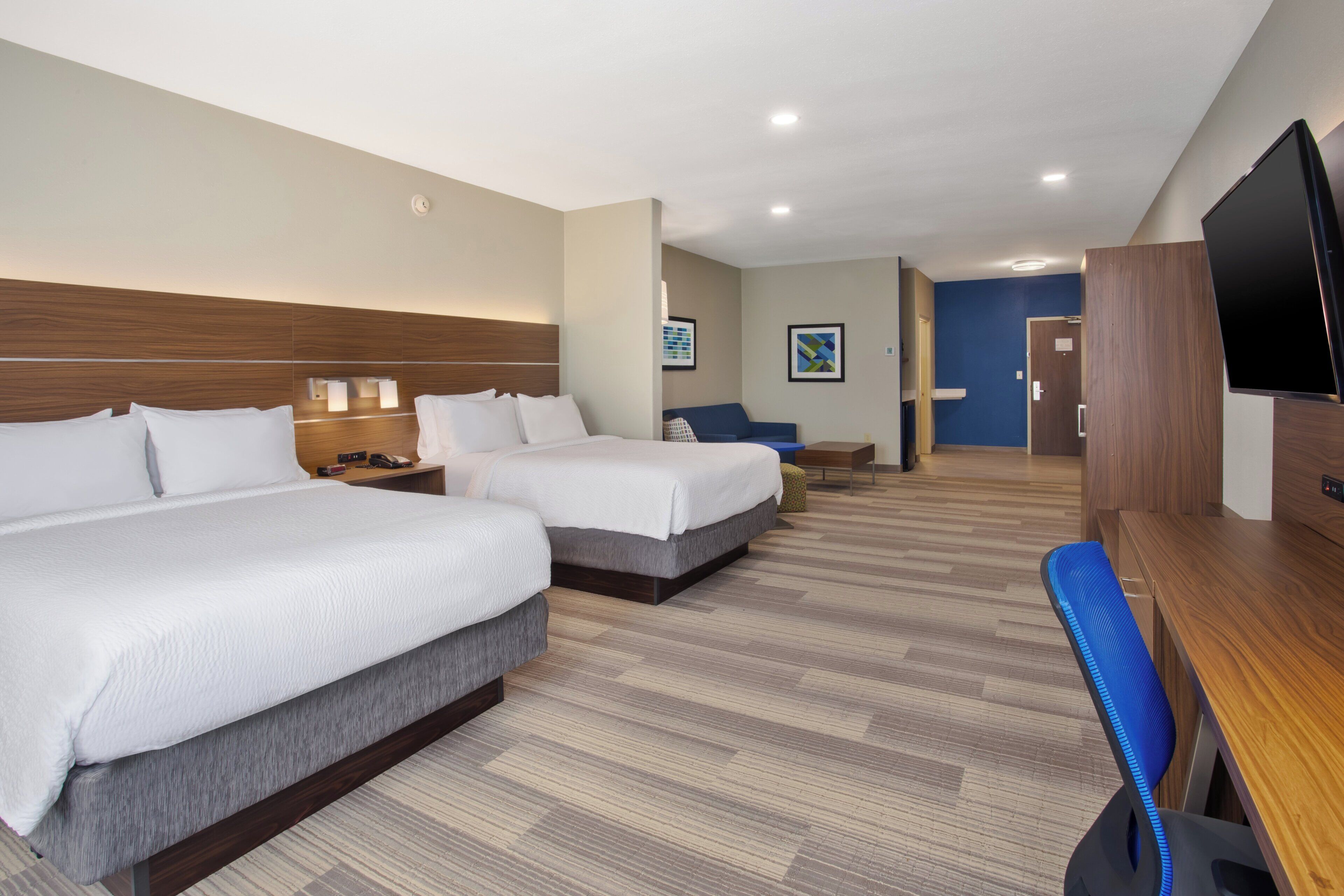A hotel room with two beds, a desk, a TV, and a bathroom visible in the background.