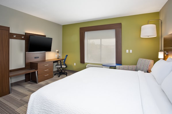 A hotel room with a bed, a desk, a chair, a television, and a window.